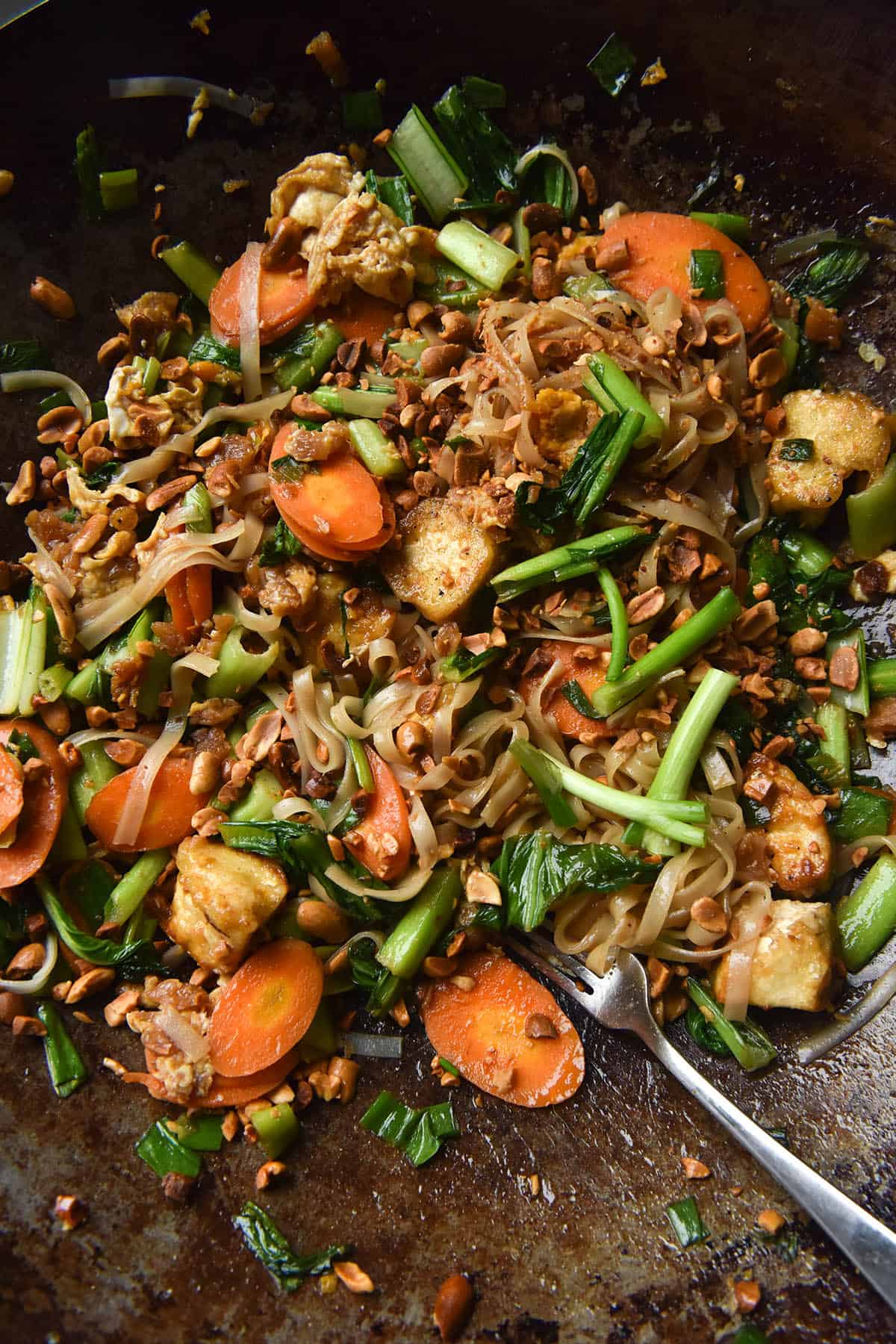 An aerial close up view of a wok filled with FODMAP friendly vegetarian Pad Thai and crispy cubes of tofu. 