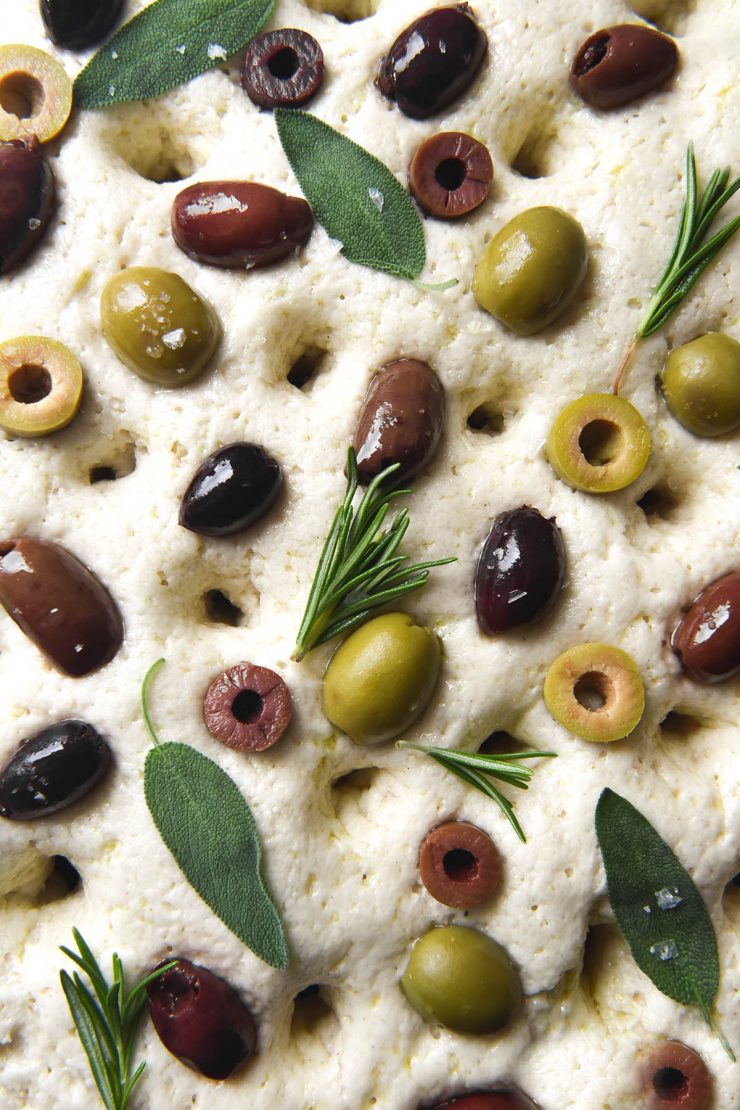 An aerial macro image of olives on an unbaked gluten free focaccia