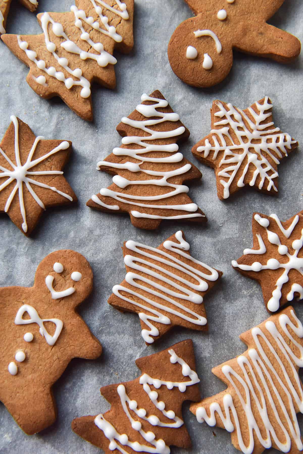 An aerial view of a tray of gluten free gingerbread cut into star, Christmas tree and gingerbread person cookies. The cookies are decorated with white icing sugar in various patterns. 