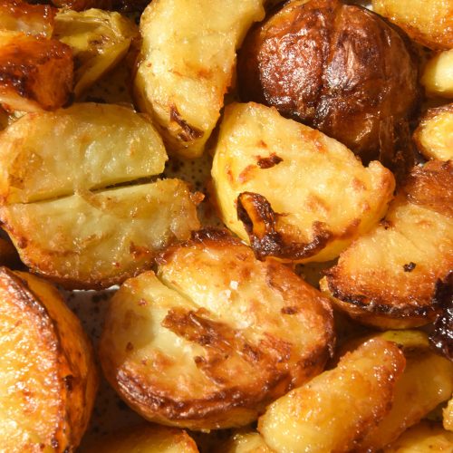 A close up aerial photo of crispy vegan roast potatoes arranged on a tray in bright sunlight