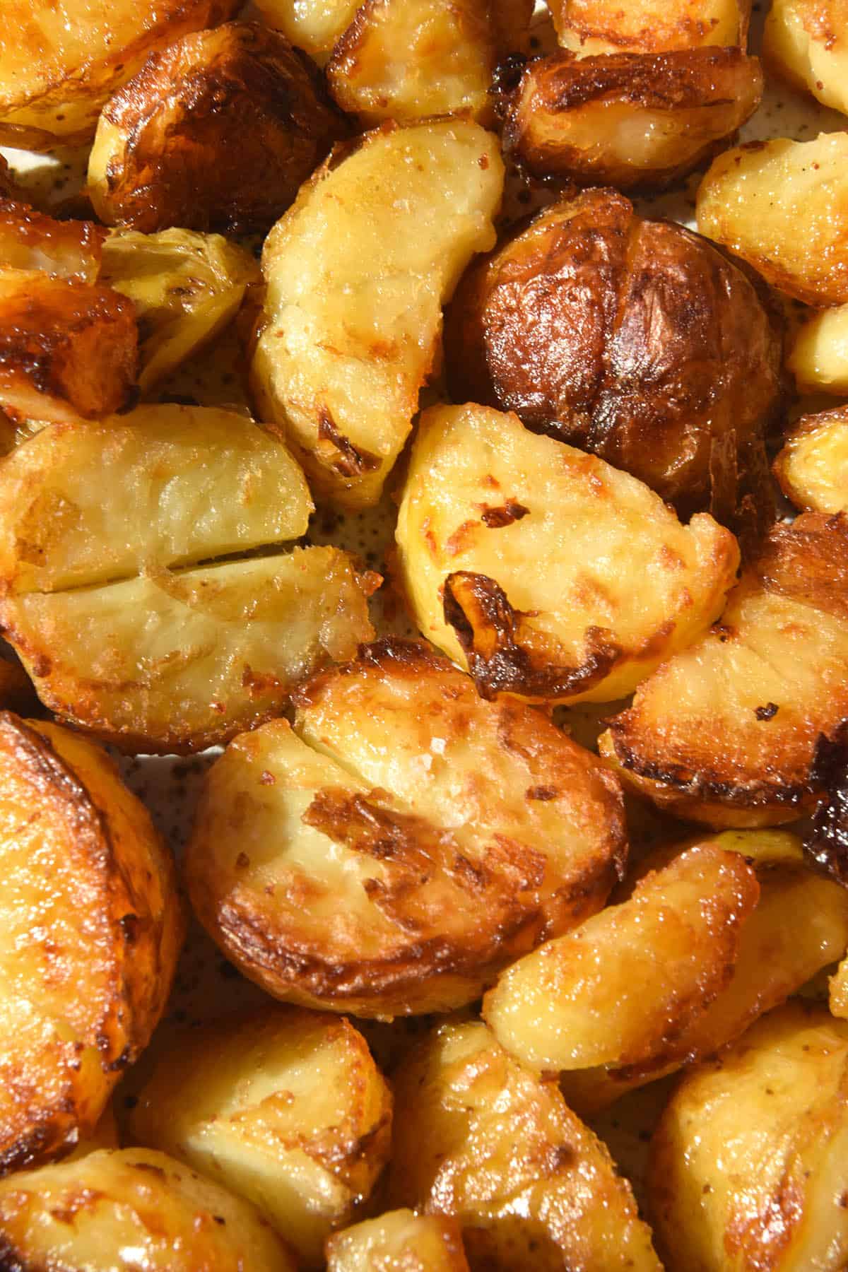 A close up aerial image of vegan roast potatoes on a white speckled ceramic plate. The potatoes are crispy, crunchy and golden brown in colour.