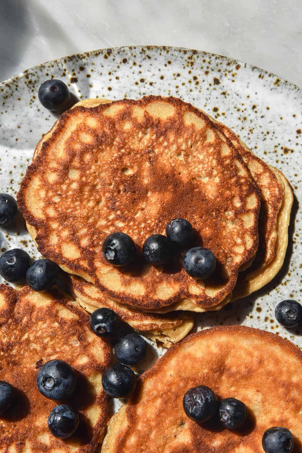 An aerial close up view of a white speckled ceramic plate topped with banana protein pancakes, which are topped with blueberries