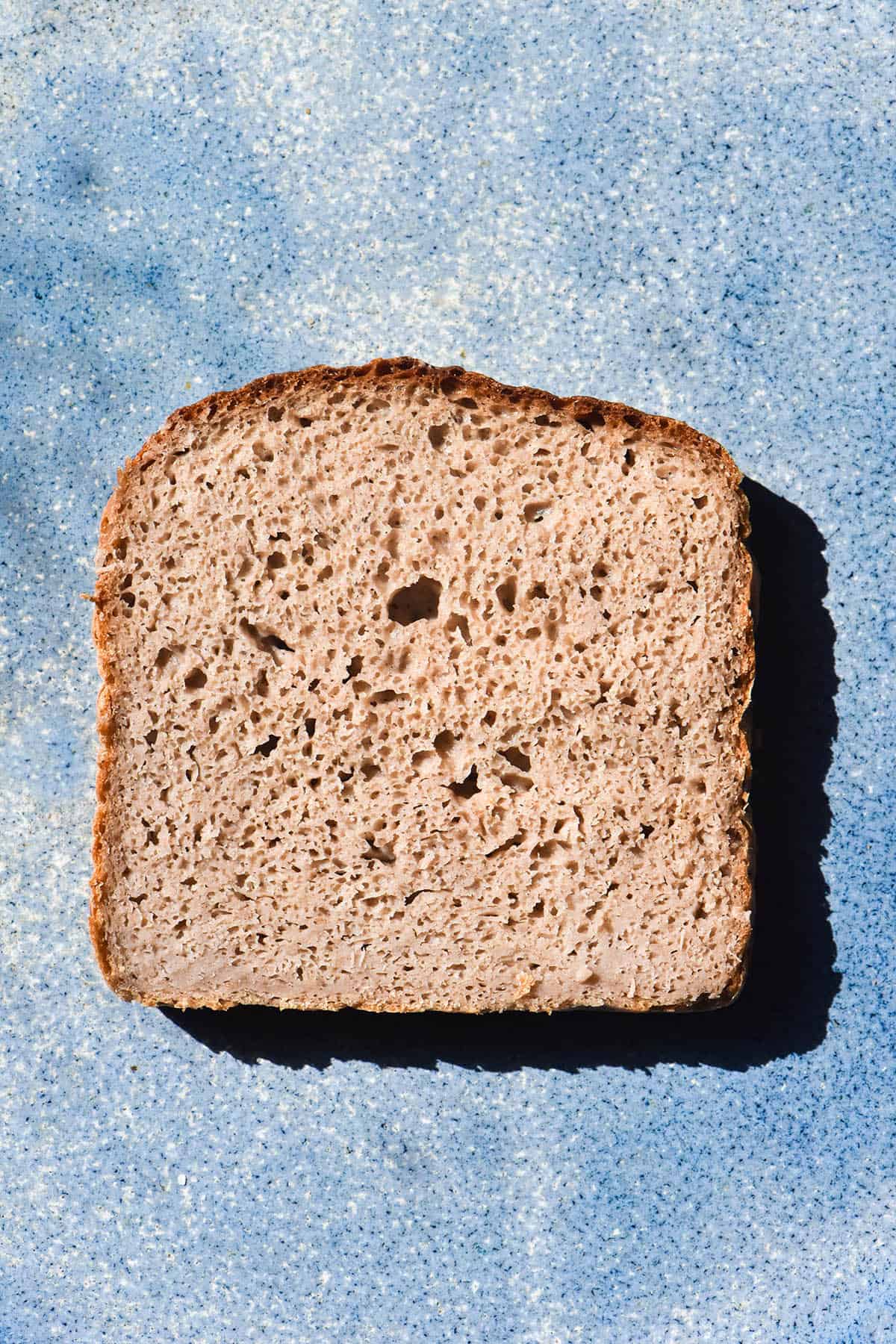 An aerial sunlit image of a slice of gluten free buckwheat bread atop a bright blue ceramic plate