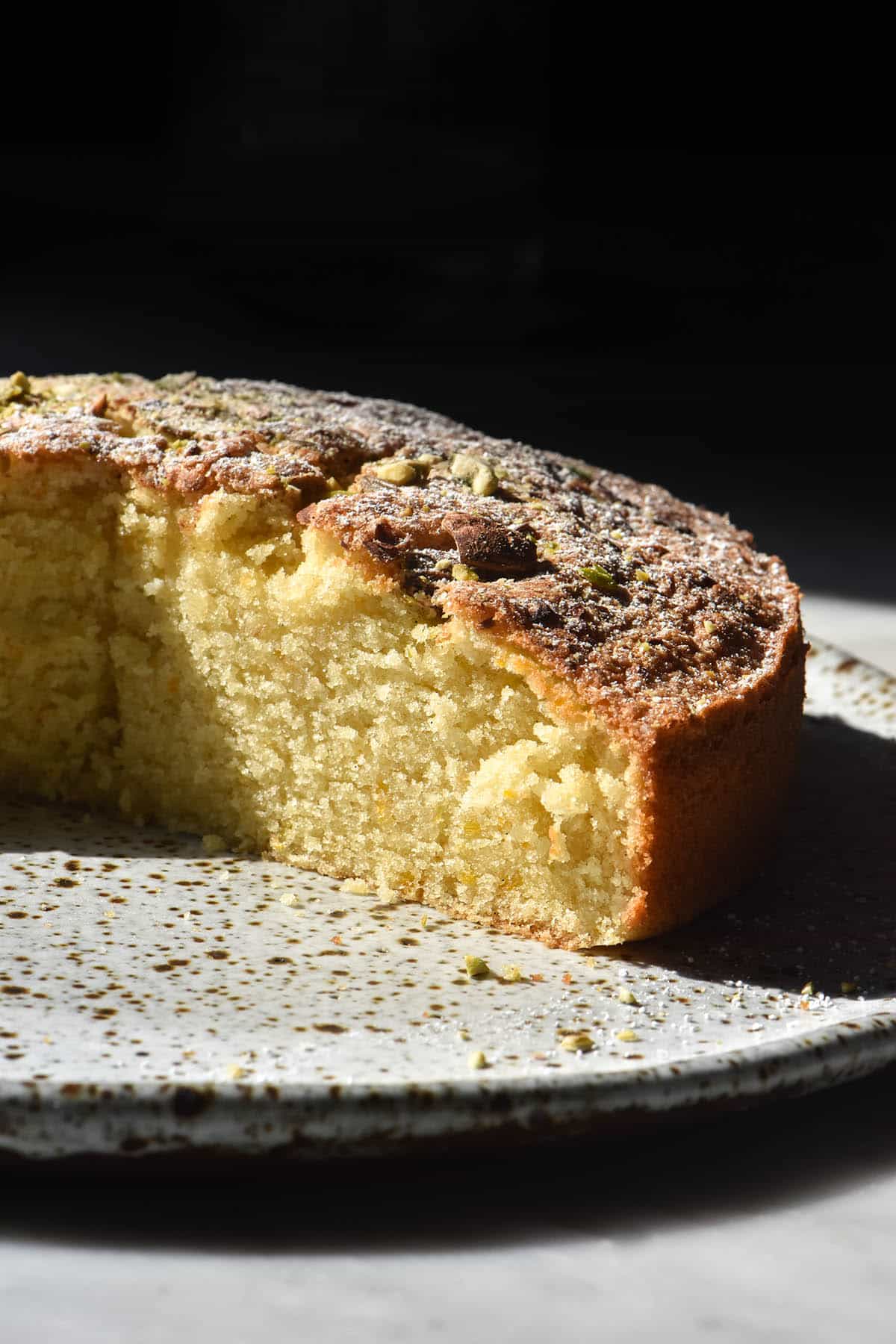 A side on image of a gluten free lemon olive oil cake in contrasting light against a black backdrop