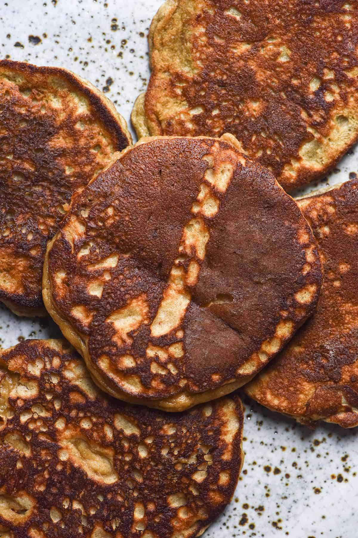 An aerial view of golden brown protein powder pancakes arranged on a white speckled ceramic plate