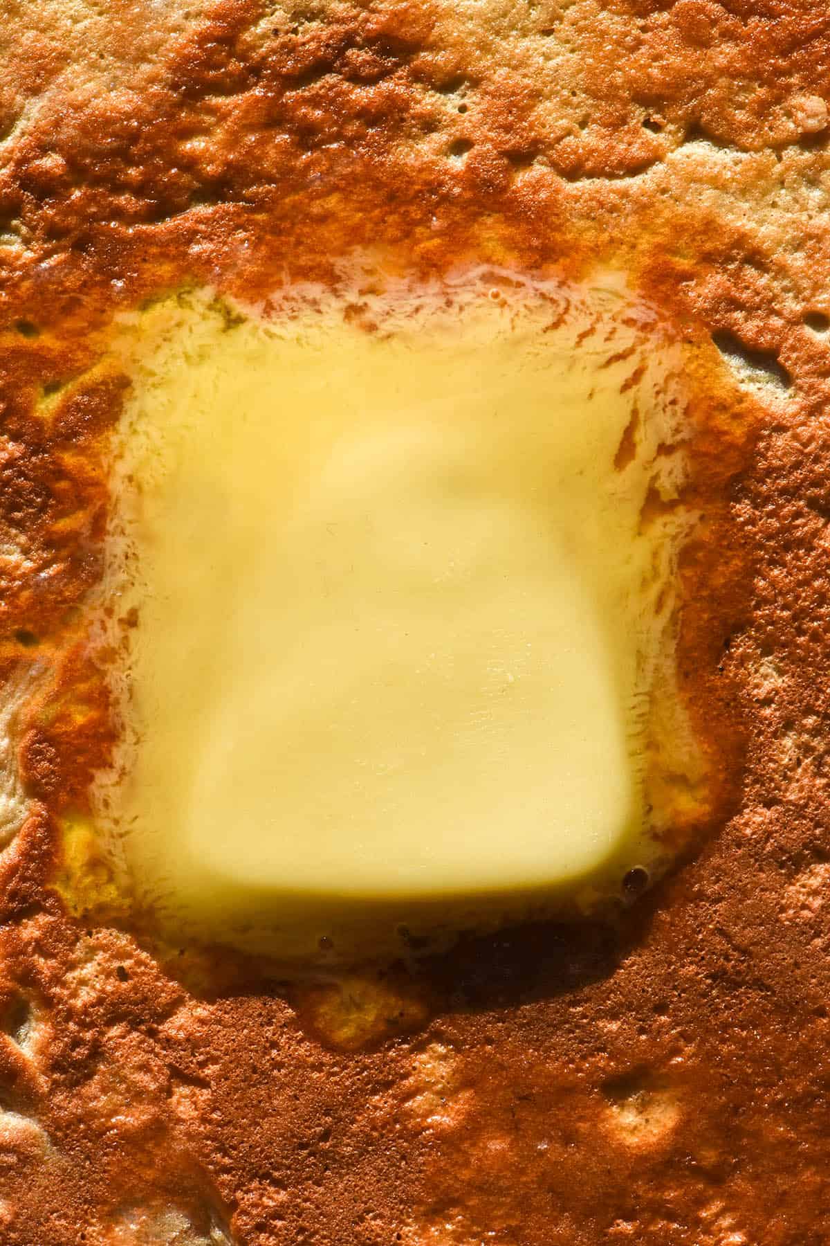 A close up macro image of a pat of butter melting on a golden brown protein pancake