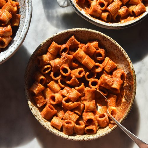 An aerial sunlit view of three bowls on a white marble table filled with tomato mascarpone pasta