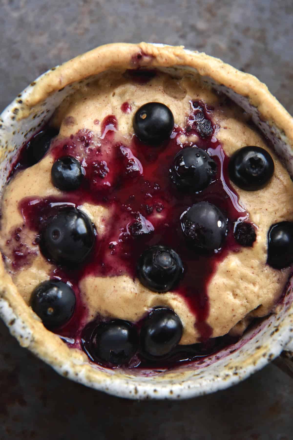 An aerial close up view of a whey protein mug cake topped with blueberries and a dark purple blueberry compote.