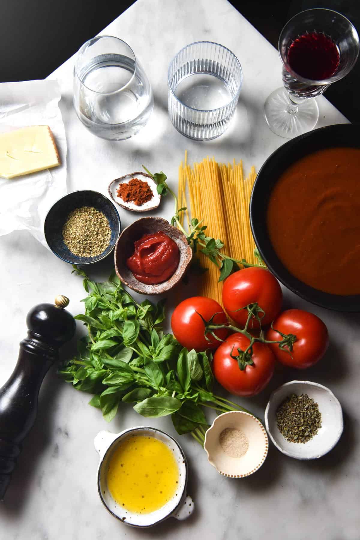 An aerial image of ingredients for a low FODMAP pasta sauce casually arranged on a white marble table. 