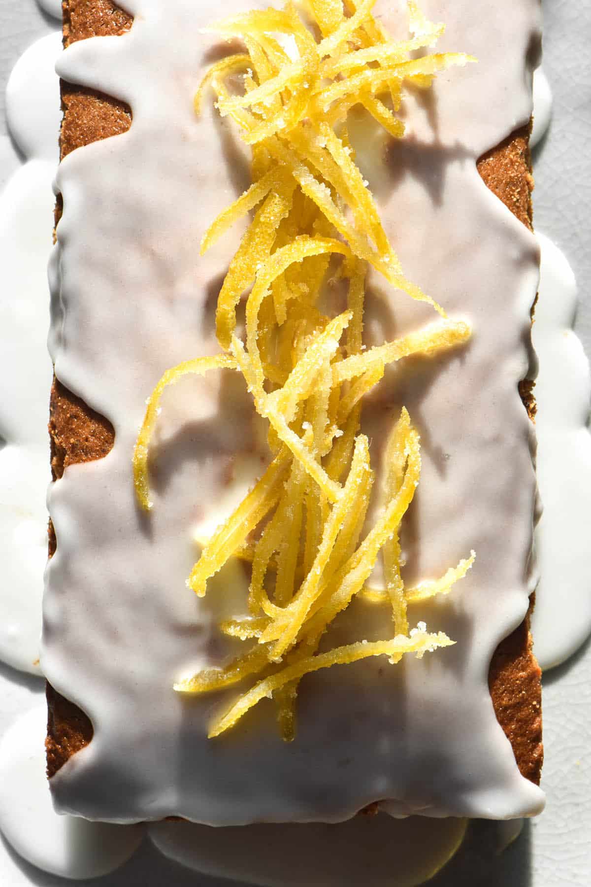 An aerial close up view of a gluten free lemon poppy seed loaf topped with lemon icing and candied lemon peel