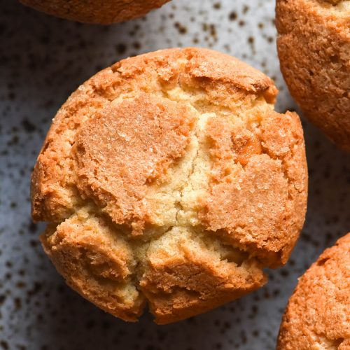 An aerial image of gluten free muffins on a white speckled ceramic plate. The muffins are finished with sanding sugar for a crispy and crunchy top.