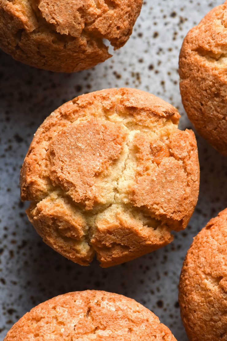 An aerial image of gluten free muffins on a white speckled ceramic plate. The muffins are finished with sanding sugar for a crispy and crunchy top.