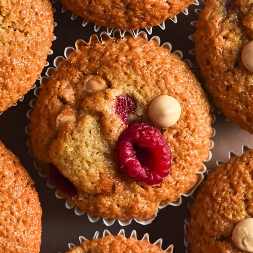 An aerial close up image of gluten free raspberry muffins topped with fresh raspberries and white chocolate chips.