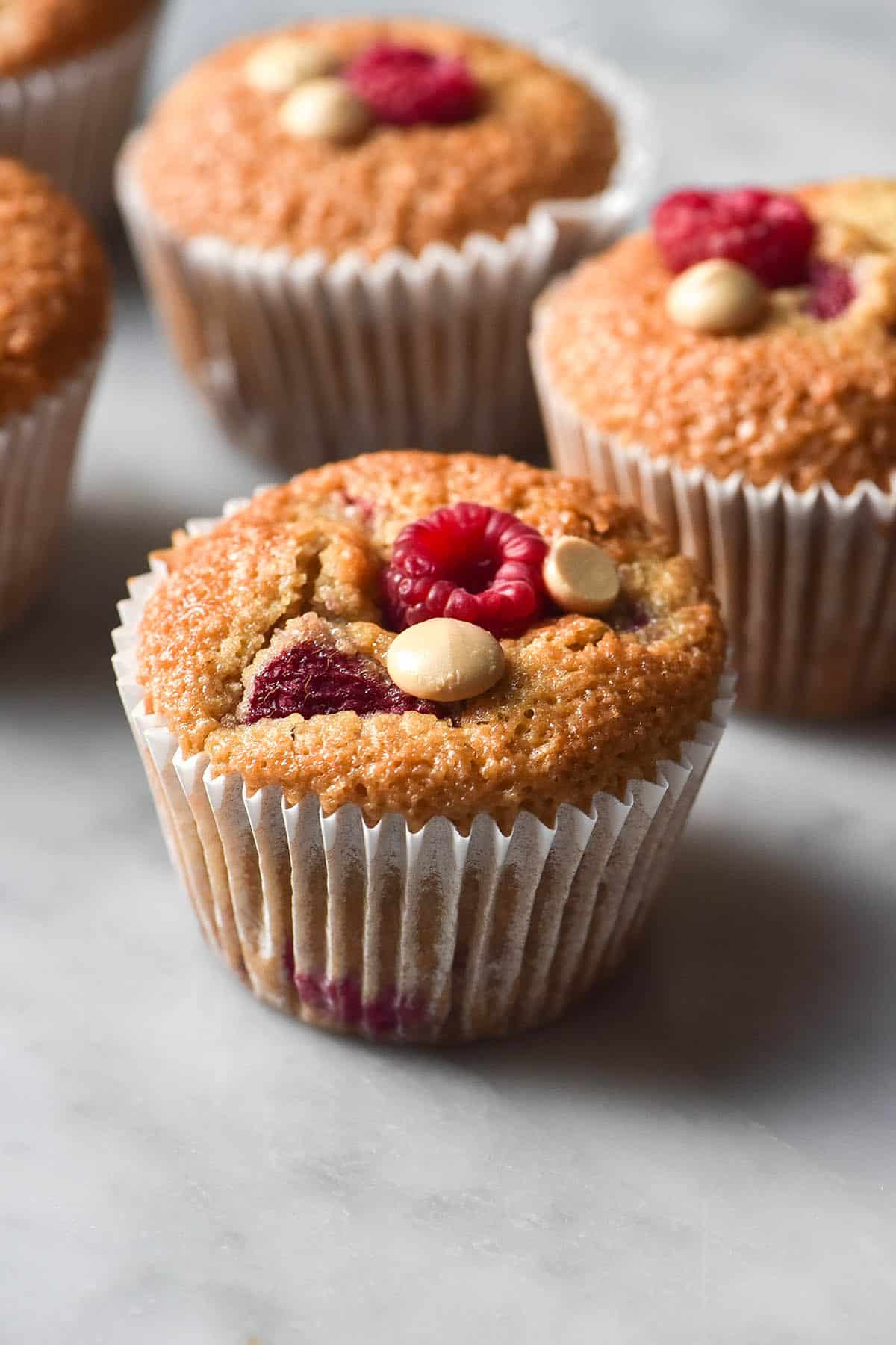 An side on view of gluten free raspberry muffins arranged casually on a white marble table