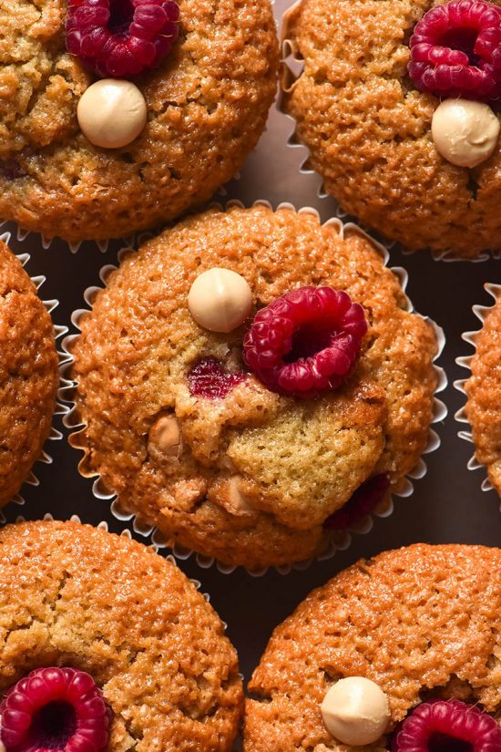 An aerial close up image of gluten free raspberry muffins topped with fresh raspberries and white chocolate chips.