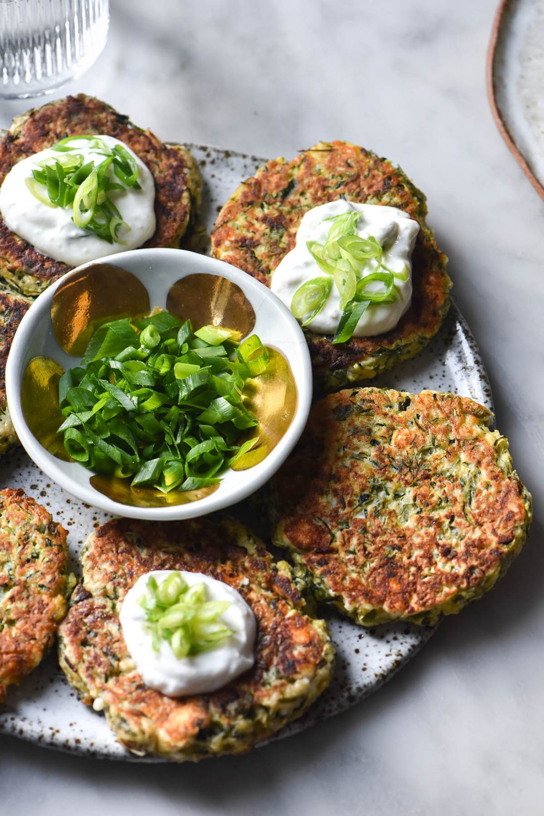 Overhead shot of a plate of golden brown gluten free zucchini fritters with herbs and dipping sauce