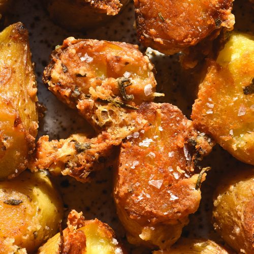 An aerial macro image of crispy roasted kipfler potatoes with a parmesan and herb crust. The potatoes are golden brown and sprinkled with sea salt flakes