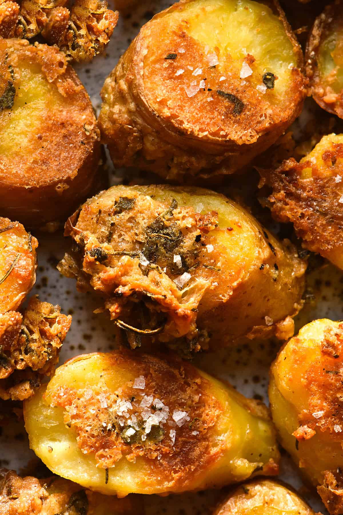 An aerial close up image of roasted kipfler potatoes with a herb and parmesan crust. The potatoes are crunchy, golden brown and topped with a sprinkle of sea salt flakes