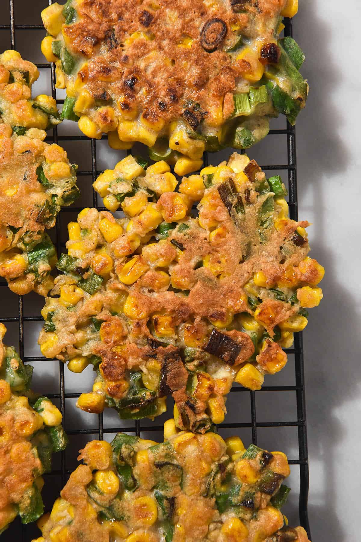 A close up aerial image of gluten free corn fritters on a wire cooling rack atop a white marble table. 