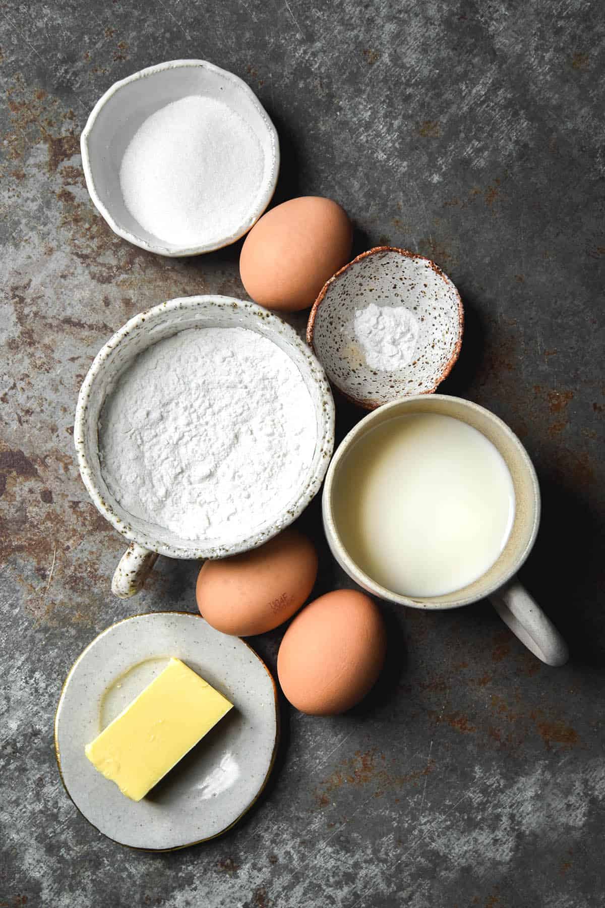 An aerial image of the ingredients for a gluten free Dutch baby on a mottled steel backdrop