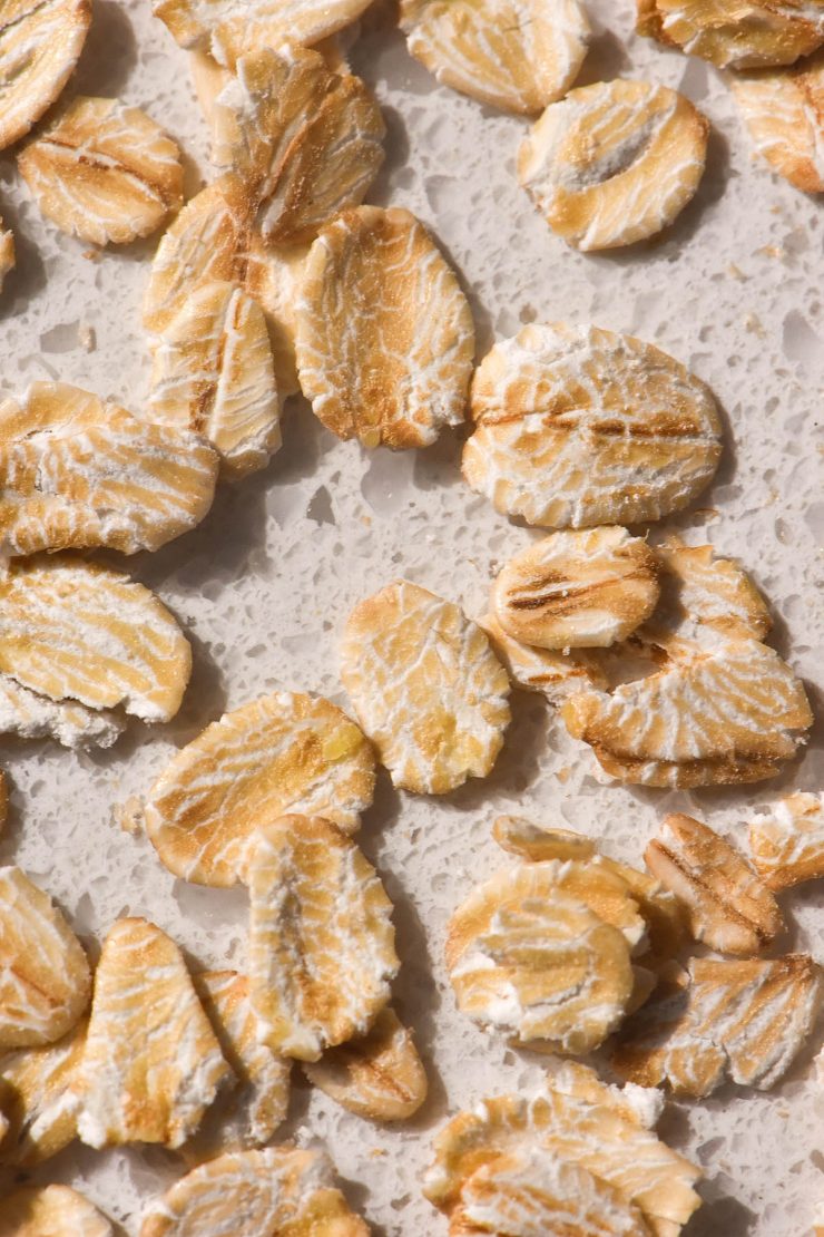 An aerial macro image of rolled oats on a white speckled stone benchtop