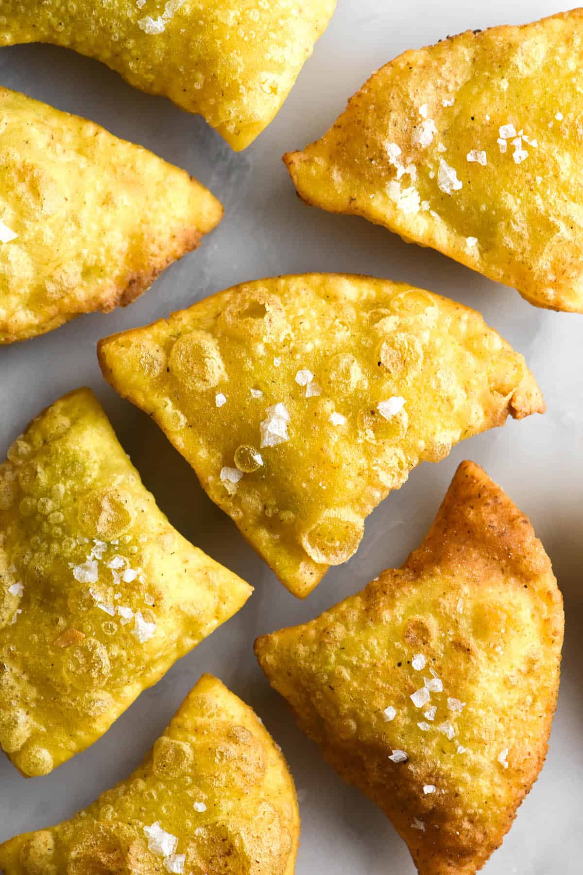 An aerial image of crispy gluten free samosas arranged casually on a white marble table