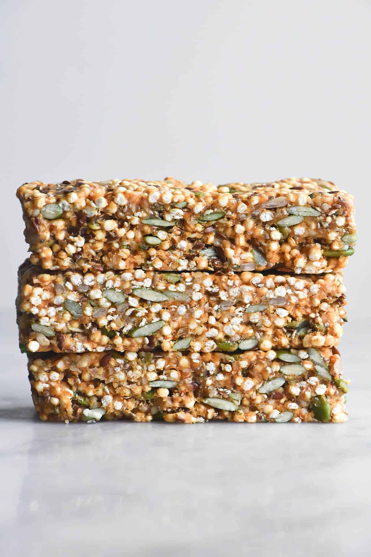 A side on image of a stack of three seedy no bake breakfast bars on a white marble table against a white backdrop