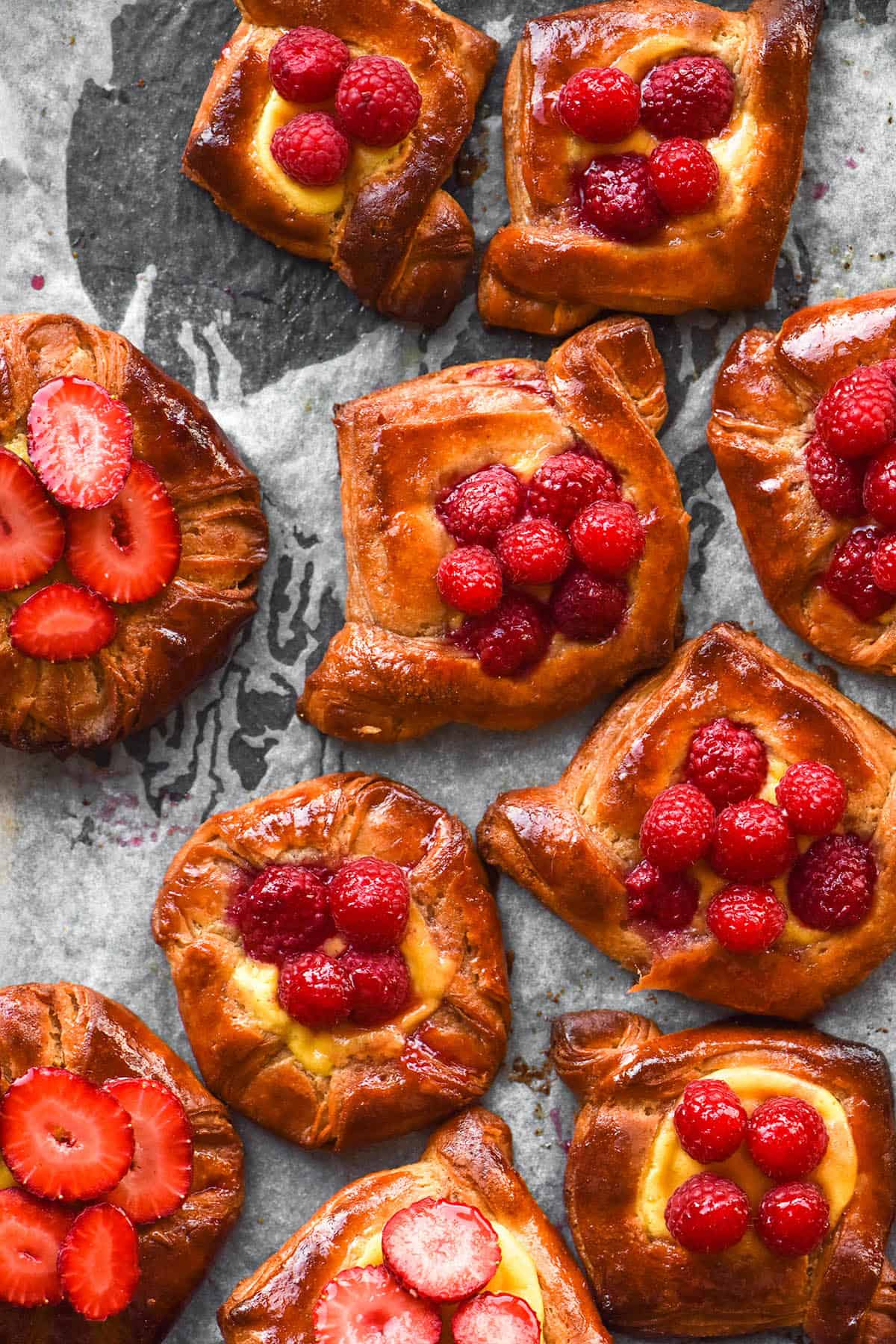 An aerial image of gluten free fruit pastries on a lined baking sheet. The pastries are filled with custard and strawberries and the outer pastry is golden brown