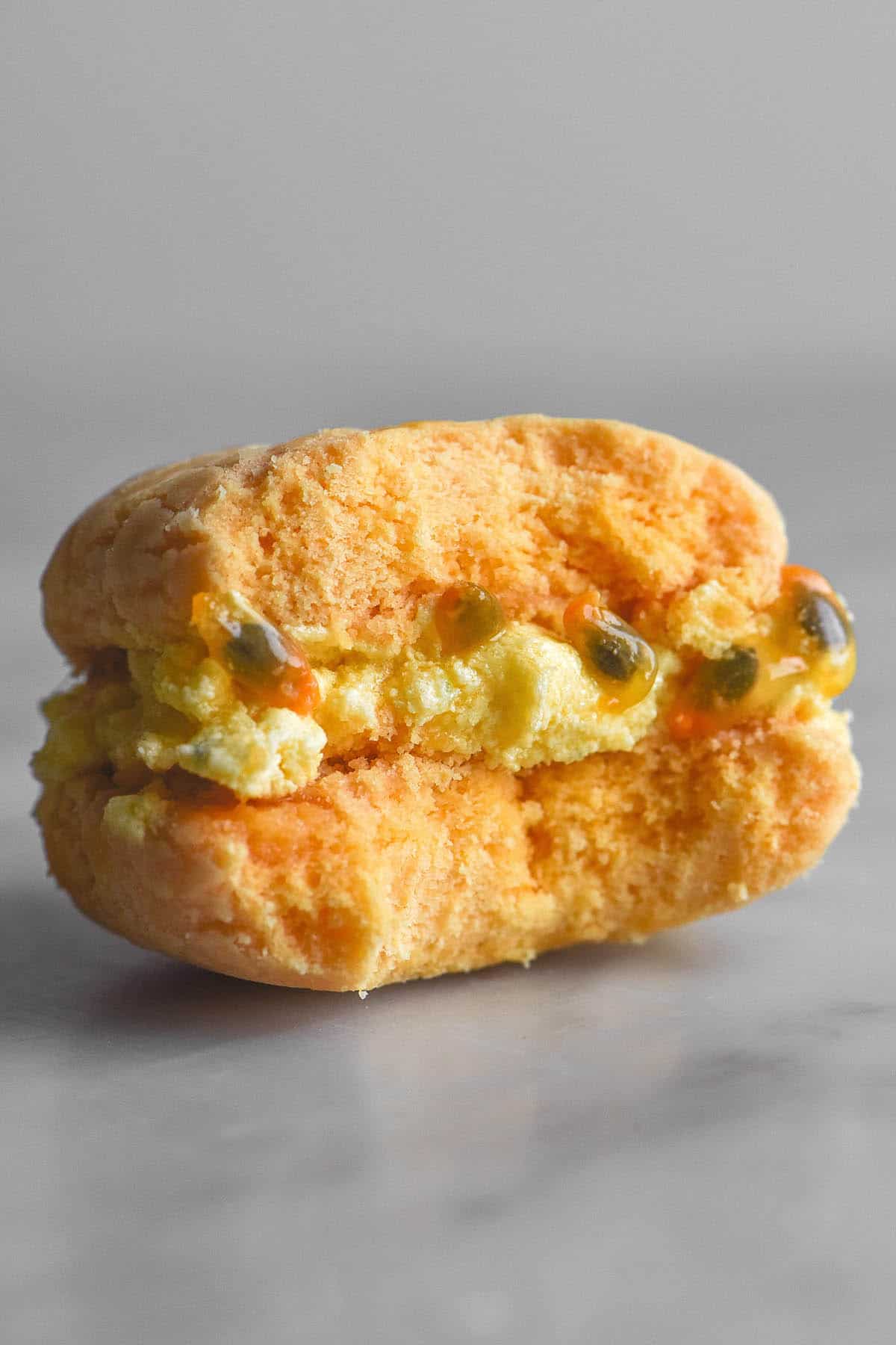 A close up image of a gluten free yoyo biscuit with a lime and passionfruit filling. The yoyo sits on a white marble table against a white backdrop