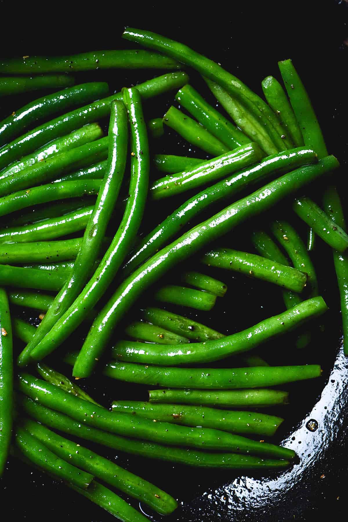 A moody image of a black pan filled with low FODMAP green beans cooked in garlic infused ghee, salt and pepper. 