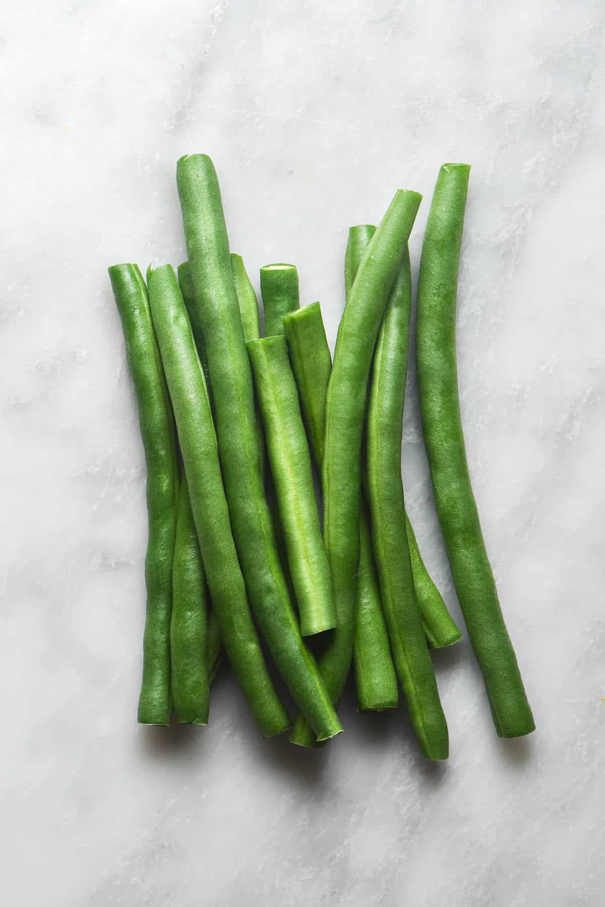 An aerial close up image of green beans on a white marble table. 