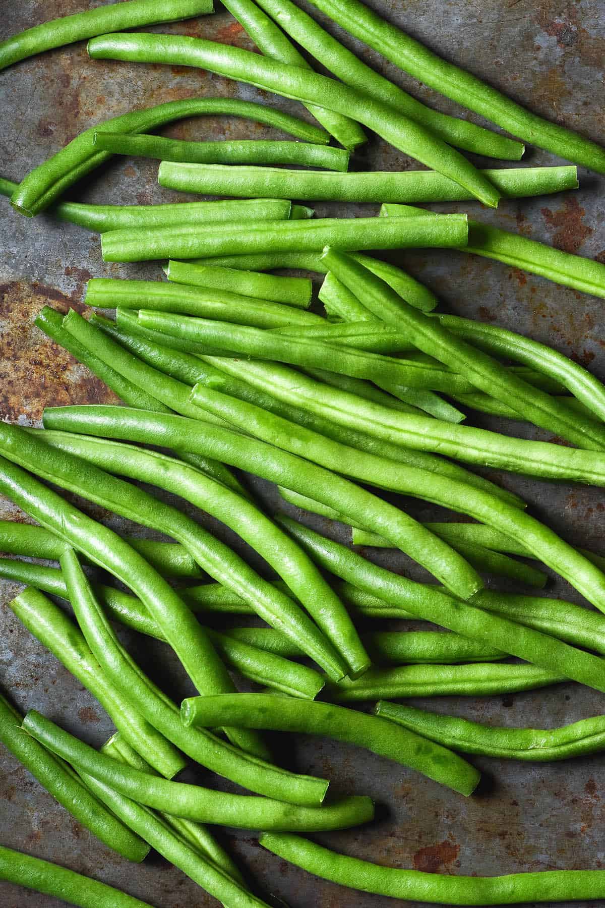 An aerial close up of raw green beans on a tectured dark steel backdrop
