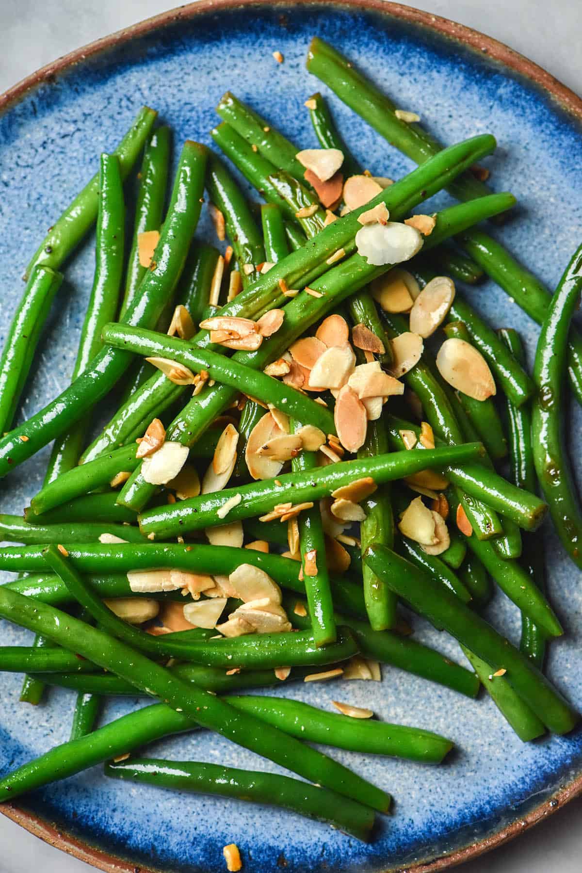 An aerial close up of a blue ceramic plate topped with low FODMAP green beans that are finished with some freshly toasted slivered almonds