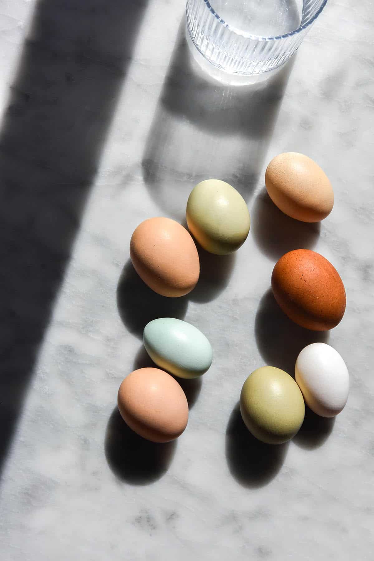 An aerial image of heirloom coloured eggs on a white marble table in contrasting sunlight