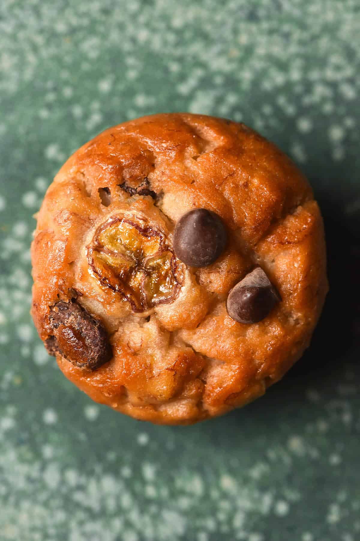 An aerial macro image of a gluten free banana choc chip muffin on a speckled green ceramic plate. 