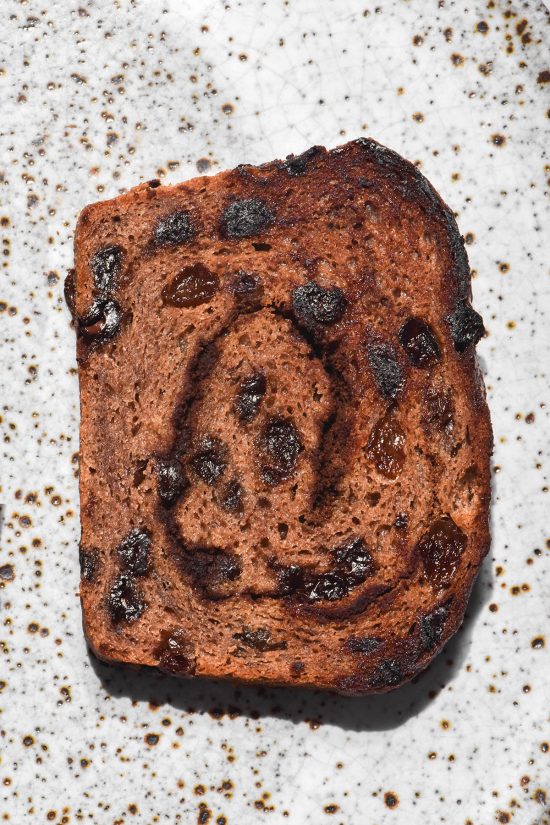 A brightly lit aerial view of a slice of gluten free vegan hot cross bun loaf, toasted and set on a white ceramic plate.