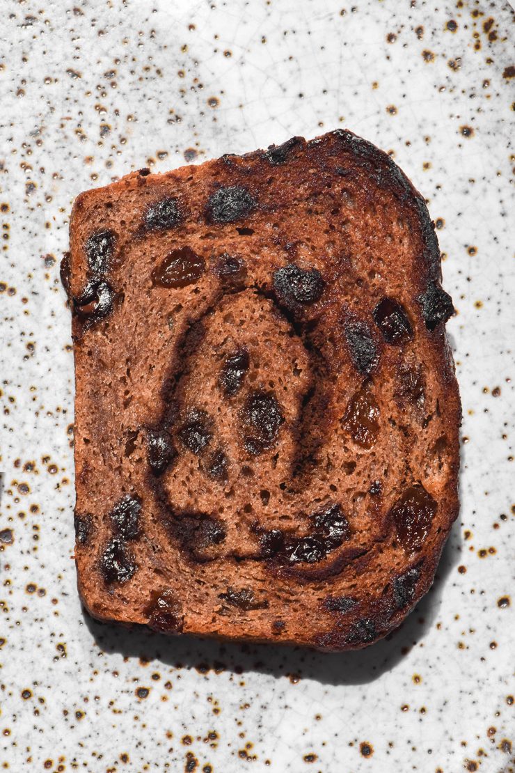A brightly lit aerial view of a slice of gluten free vegan hot cross bun loaf, toasted and set on a white ceramic plate.