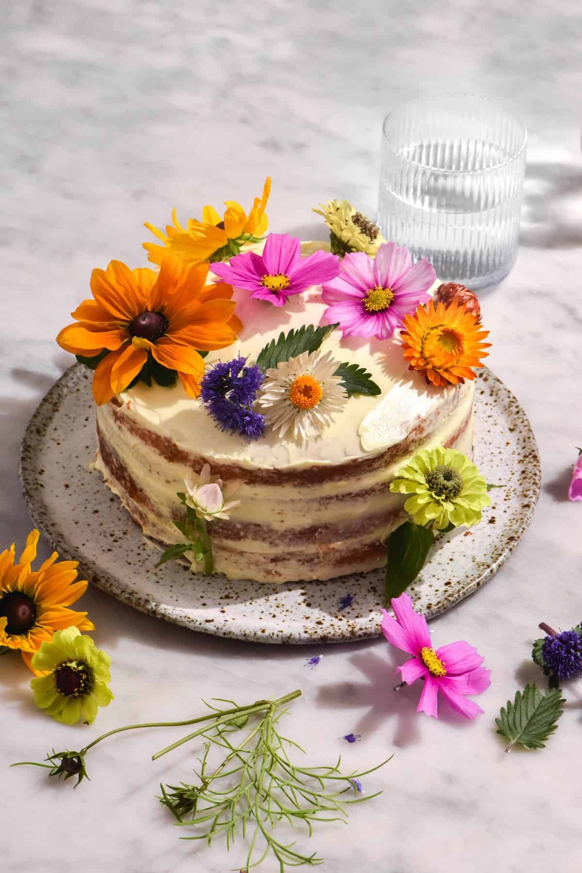 A gluten free passionfruit curd layer cake topped with multi coloured flowers on a white marble table