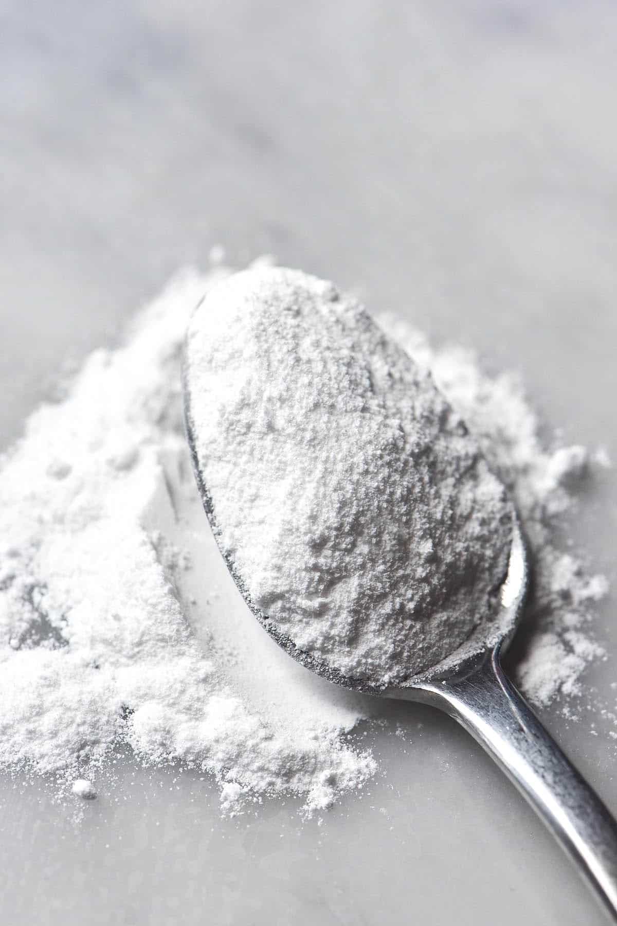 A macro image of a teaspoon filled with gluten free baking powder on a white marble table