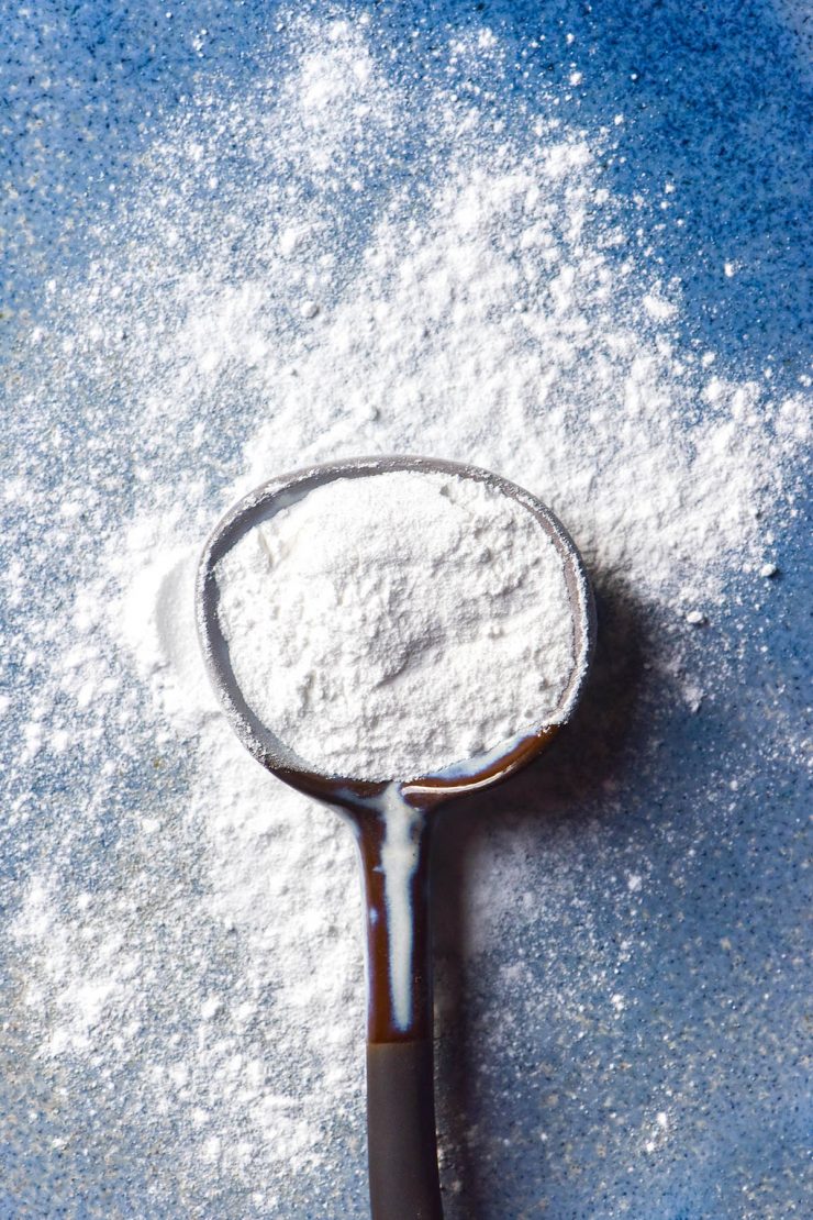 An aerial image of a ceramic spoon filled with gluten free baking powder on a sky blue ceramic plate