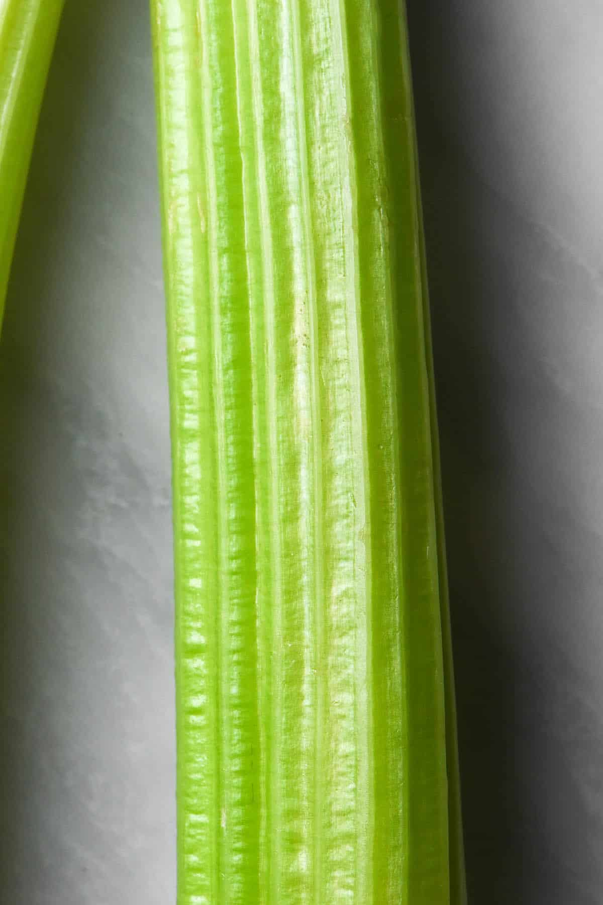 A close up macro image of a stalk of bright green celery on a white marble table. 