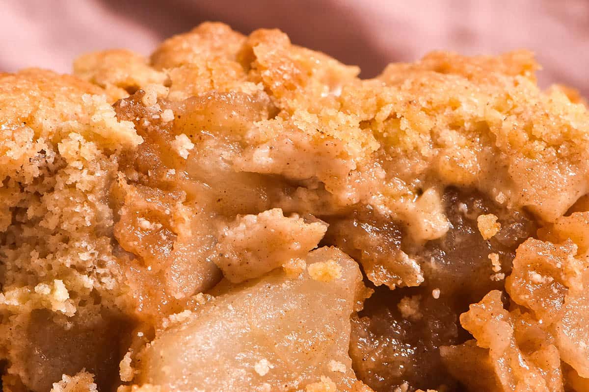 A close macro image of a piece of low FODMAP apple crumble against a pale pink backdrop