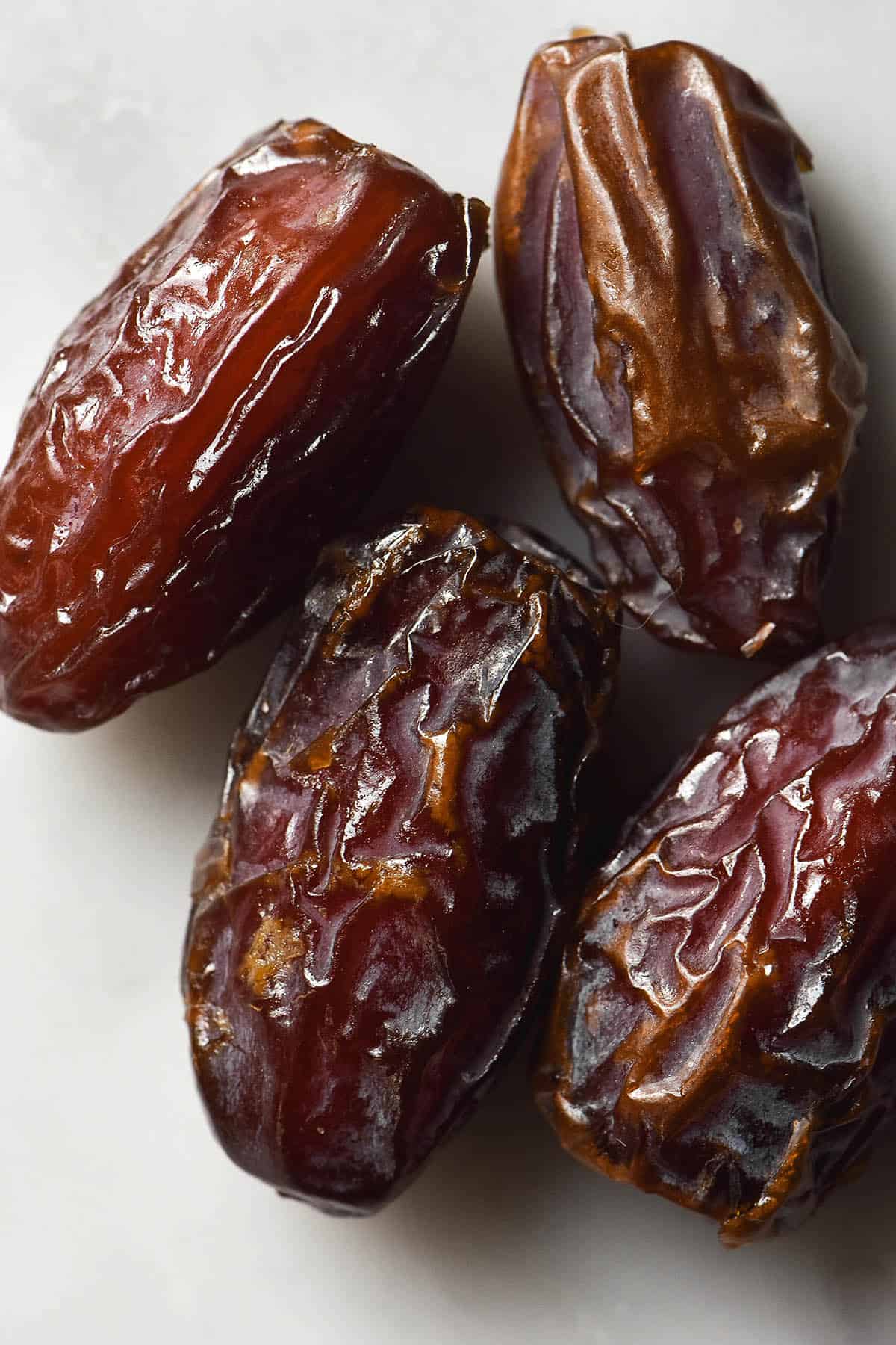 An aerial close up image of four Medjool dates on a white marble table