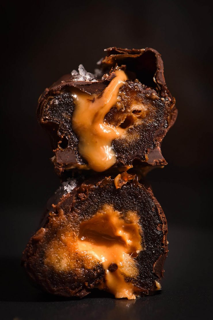 A side on close up of a peanut butter stuffed date coated in chocolate. The date has been sliced in half to reveal the nut butter innards.