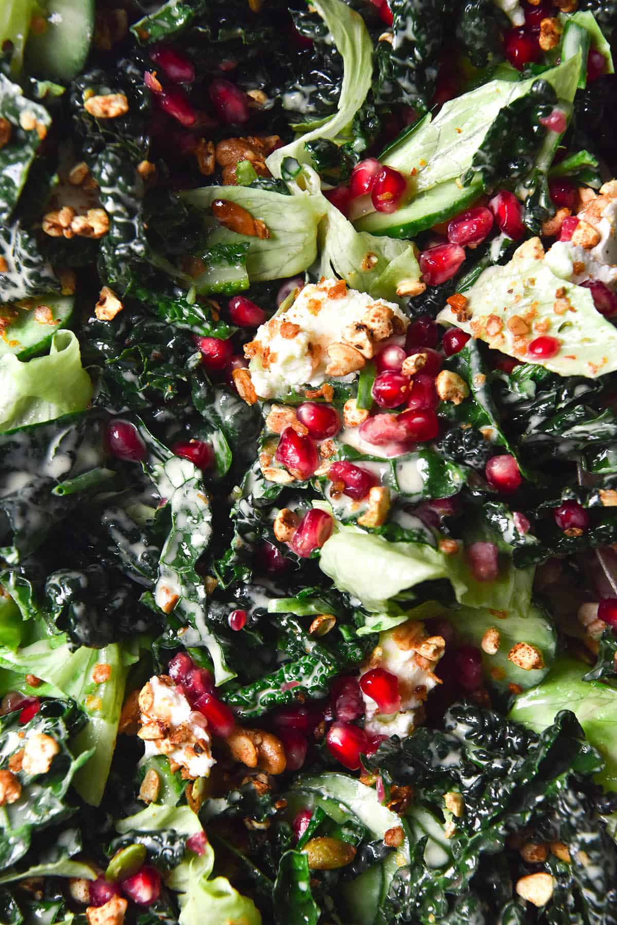 An aerial close up image of a kale salad with pomegranate, goat's cheese, lettuce, cucumber and a low FODMAP tahini dressing. 