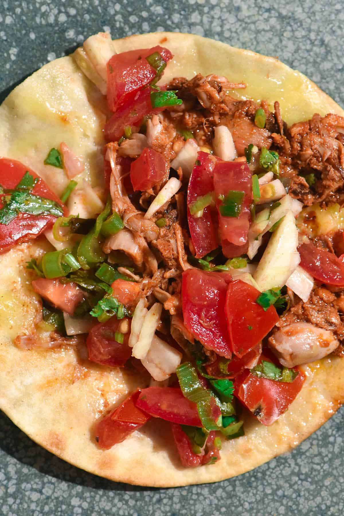 An aerial close up image of a low FODMAP jackfruit taco topped with low FODMAP pico de gallo. The taco sits open faced on a speckled ceramic green plate. 