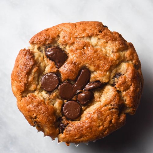 An aerial image of a gluten free banana choc chip muffin on a white marble table