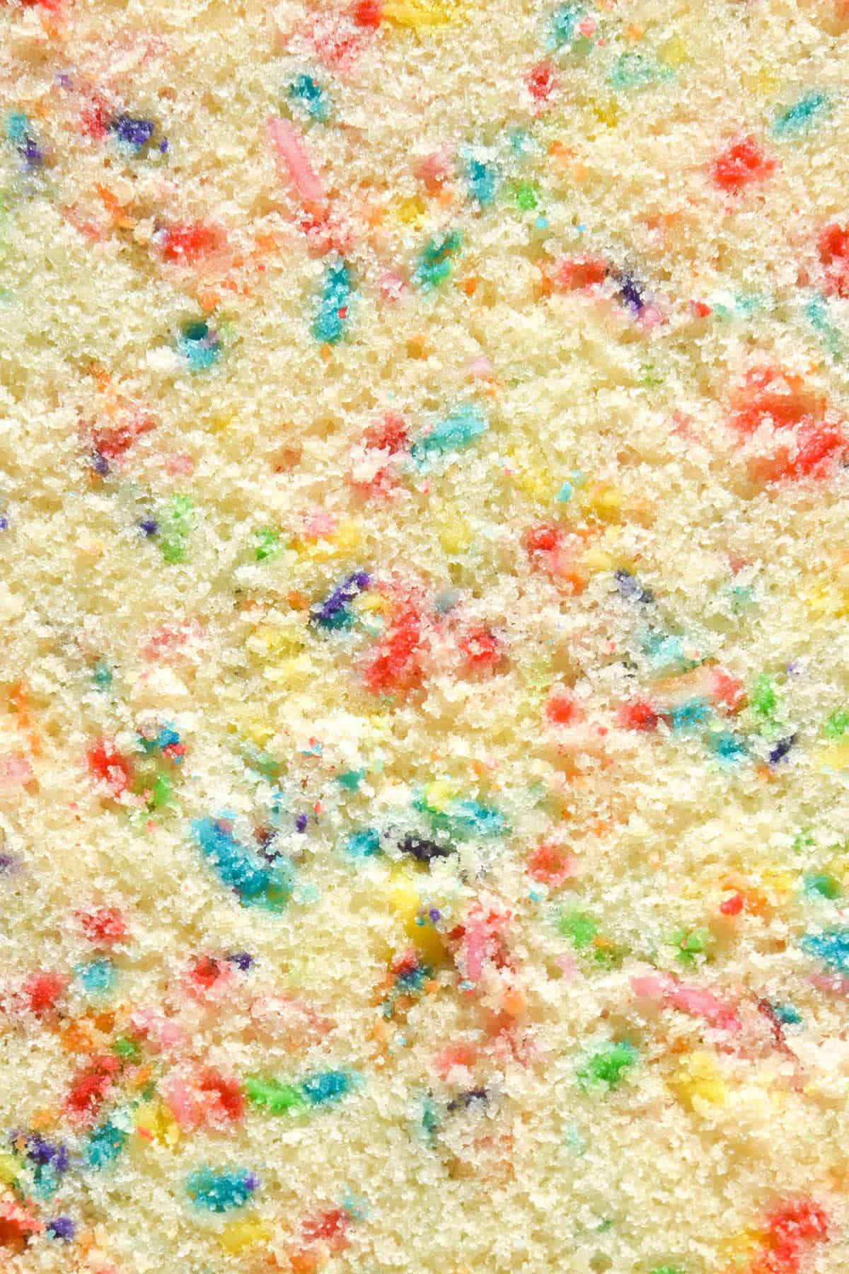 An aerial macro image of the crumb of a gluten free funfetti cake. It is light and fluffy and dotted with rainbow sprinkles