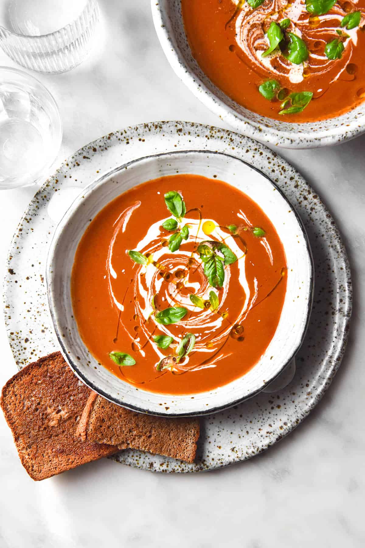 An aerial image of two bowls of low FODMAP tomato soup on a white marble table.