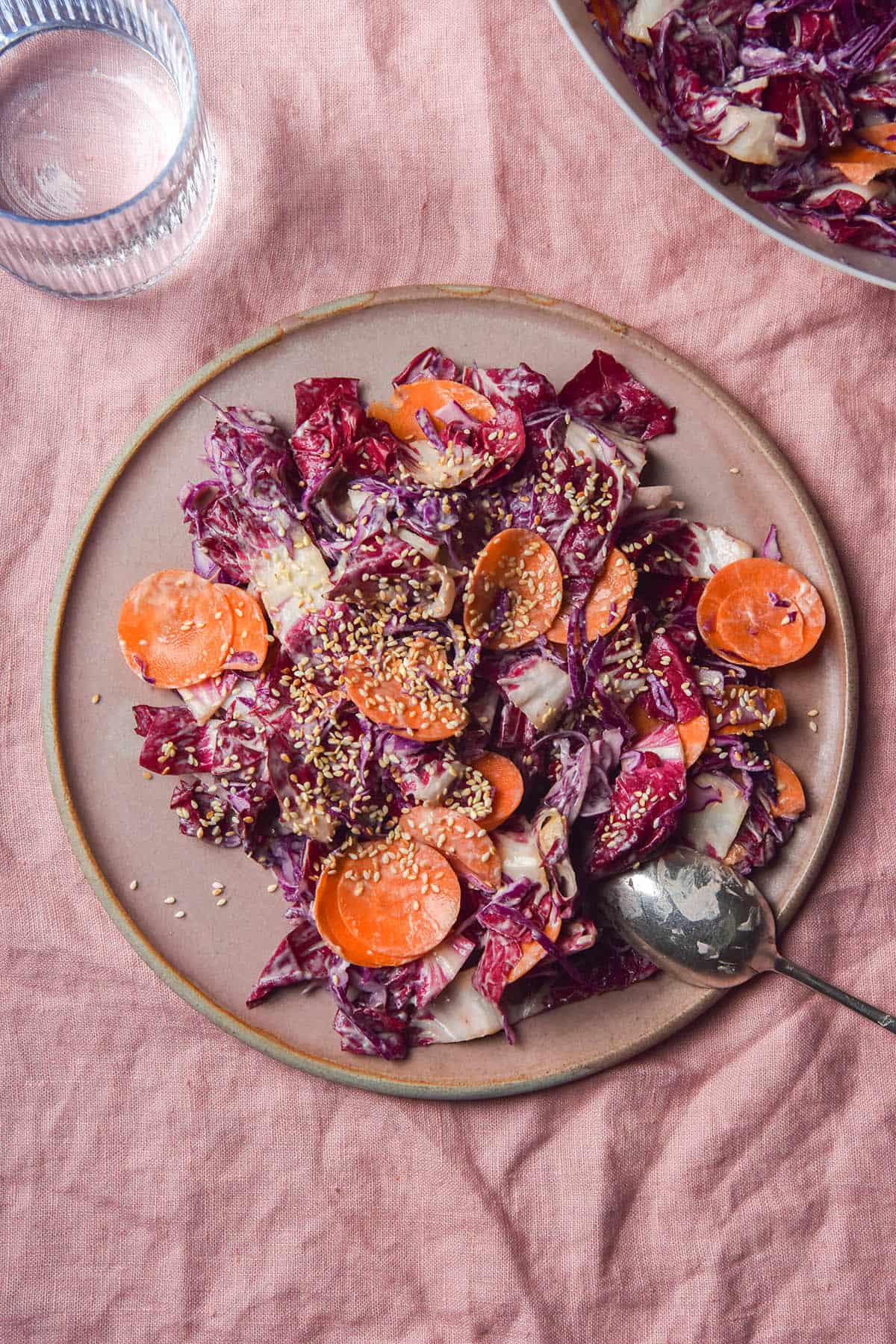 An aerial image of a red cabbage and radicchio coleslaw on a pale pink plate atop a pale pink linen tablecloth. 
